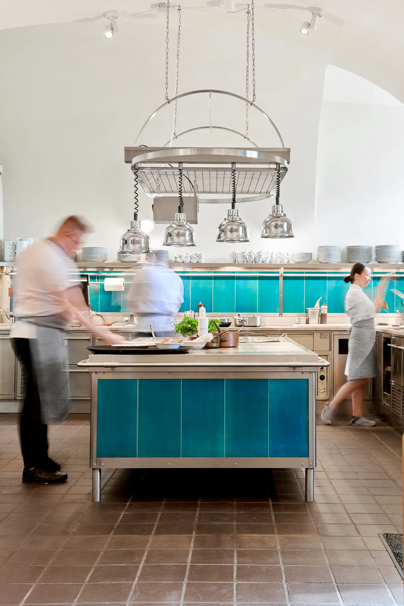 Otevřená restauranční kuchyně s kuchaři při práci a centrálním pracovním stolem.